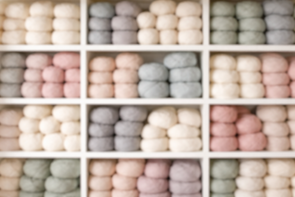 [light] Baggrund til udtalelser: et mere afdæmpet, ensartet billede af garnhylder i bløde farver, let ude af fokus, så tekst kan stå ovenpå. Det skal give tekstur og stemning uden at stjæle opmærksomheden.